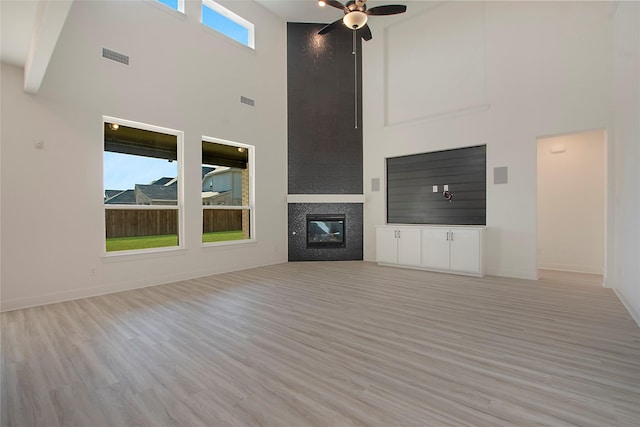 unfurnished living room featuring light hardwood / wood-style flooring, a fireplace, ceiling fan, and a high ceiling