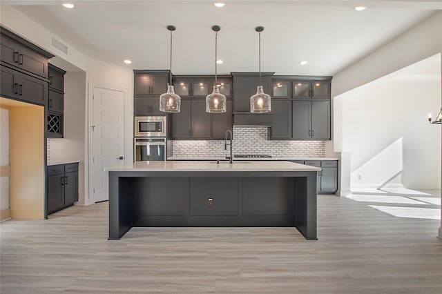 kitchen with hanging light fixtures, appliances with stainless steel finishes, a kitchen island with sink, and backsplash