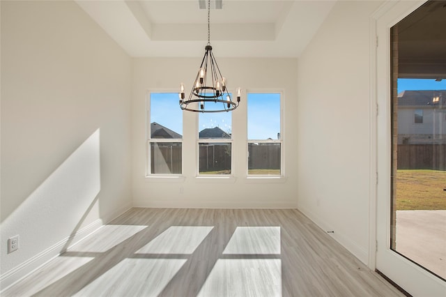 unfurnished dining area featuring a chandelier, a raised ceiling, and light hardwood / wood-style floors