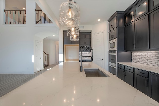 kitchen with pendant lighting, sink, stainless steel microwave, light stone countertops, and decorative backsplash