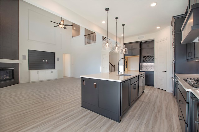 kitchen with decorative light fixtures, ventilation hood, an island with sink, sink, and ceiling fan