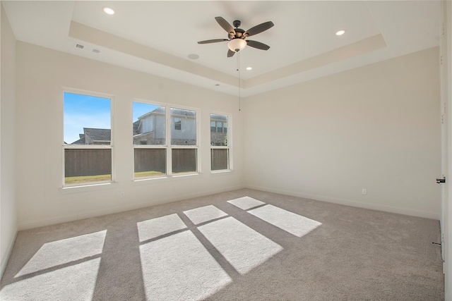 carpeted spare room featuring a tray ceiling and ceiling fan