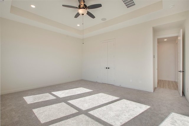 empty room with light colored carpet, a raised ceiling, and ceiling fan