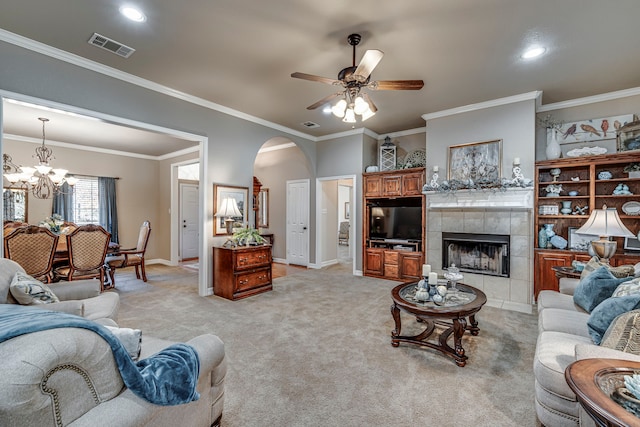 living room with crown molding, ceiling fan with notable chandelier, light colored carpet, and a fireplace