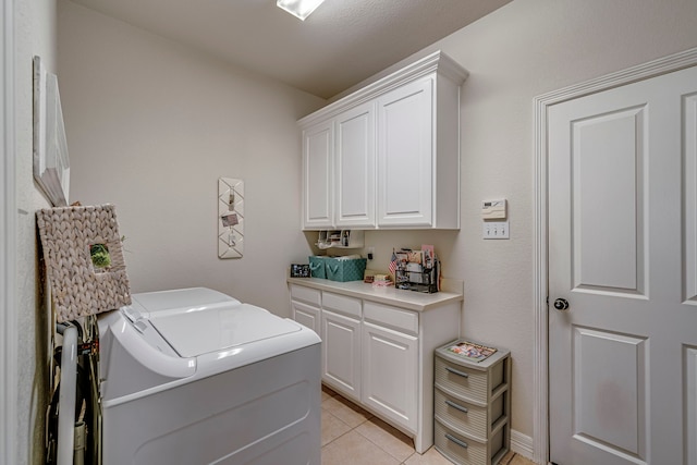 clothes washing area with washer and clothes dryer, cabinets, and light tile patterned flooring