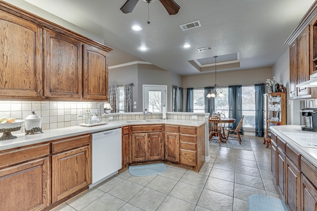 kitchen with sink, backsplash, white dishwasher, pendant lighting, and ceiling fan with notable chandelier