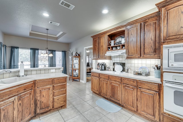 kitchen with light tile patterned flooring, pendant lighting, decorative backsplash, a raised ceiling, and white appliances