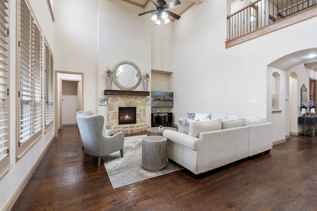 living room with dark hardwood / wood-style floors, ceiling fan, a stone fireplace, and a towering ceiling