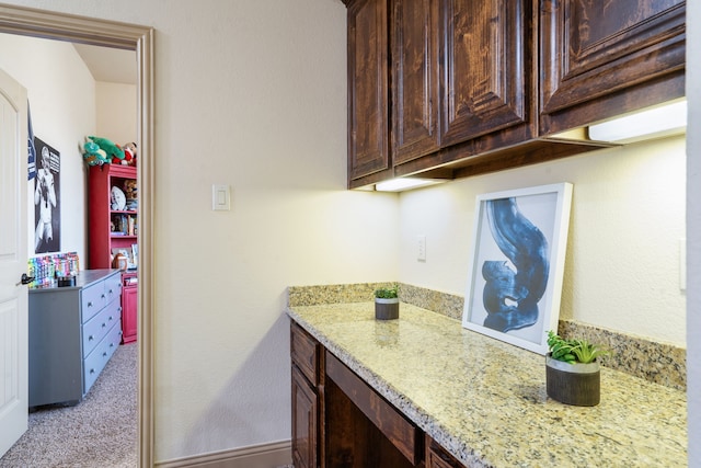 kitchen with dark brown cabinets, light stone countertops, and light carpet