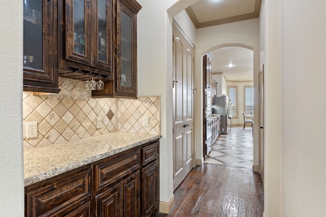 kitchen with tasteful backsplash, ornamental molding, light stone countertops, and dark brown cabinets