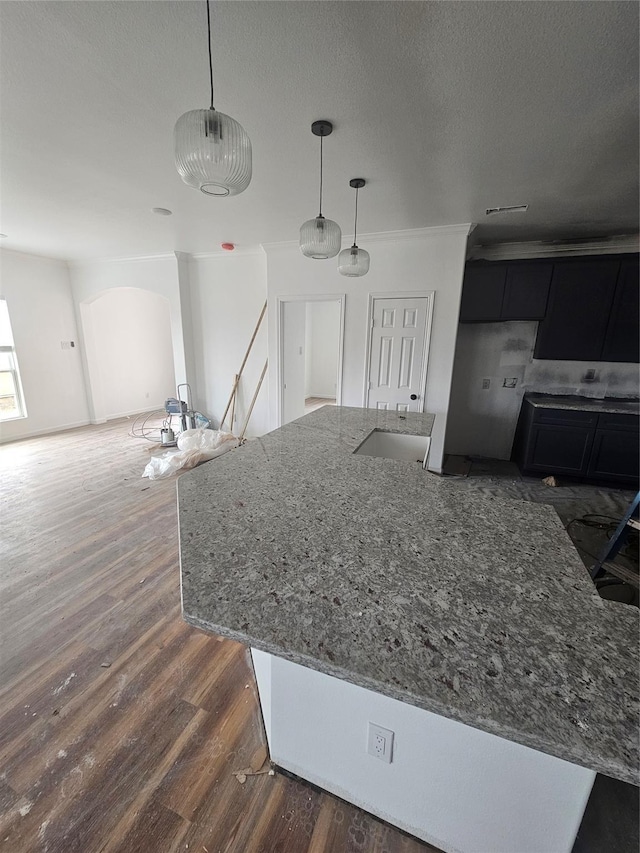 kitchen with light stone counters, dark hardwood / wood-style floors, pendant lighting, a textured ceiling, and ornamental molding