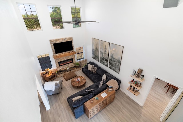 living room with a high ceiling, light hardwood / wood-style flooring, ceiling fan, and a stone fireplace