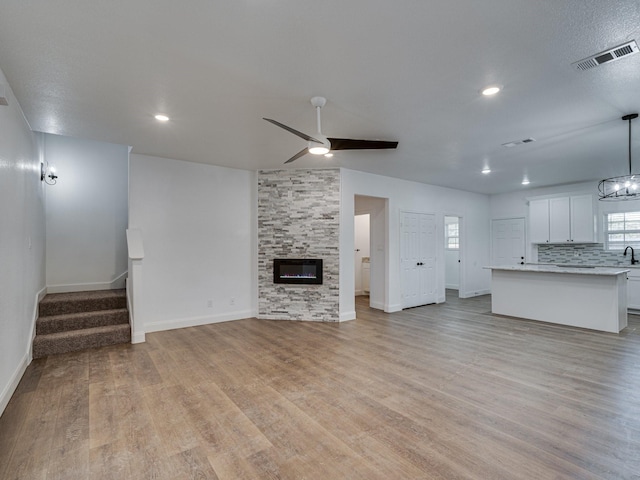 unfurnished living room with ceiling fan, a fireplace, light hardwood / wood-style floors, and sink