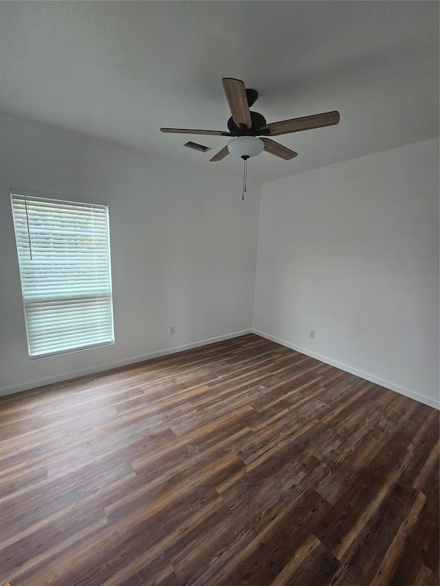 empty room featuring visible vents, a ceiling fan, baseboards, and dark wood-style flooring
