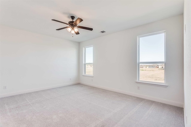 spare room featuring light carpet, ceiling fan, visible vents, and baseboards