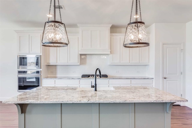 kitchen with appliances with stainless steel finishes, a kitchen island with sink, hanging light fixtures, and white cabinets