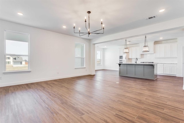 unfurnished living room with a sink, wood finished floors, visible vents, and baseboards