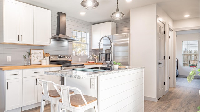 kitchen featuring a breakfast bar, white cabinets, stainless steel appliances, and wall chimney exhaust hood