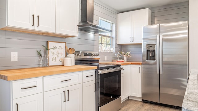 kitchen with wood counters, light wood-type flooring, stainless steel appliances, wall chimney range hood, and white cabinets