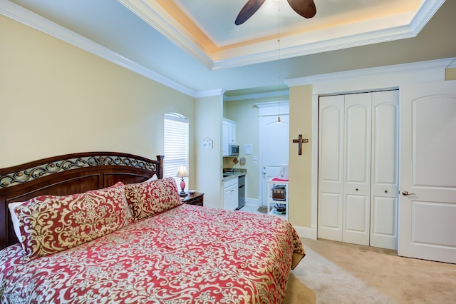 carpeted bedroom with a closet, crown molding, ceiling fan, and a tray ceiling