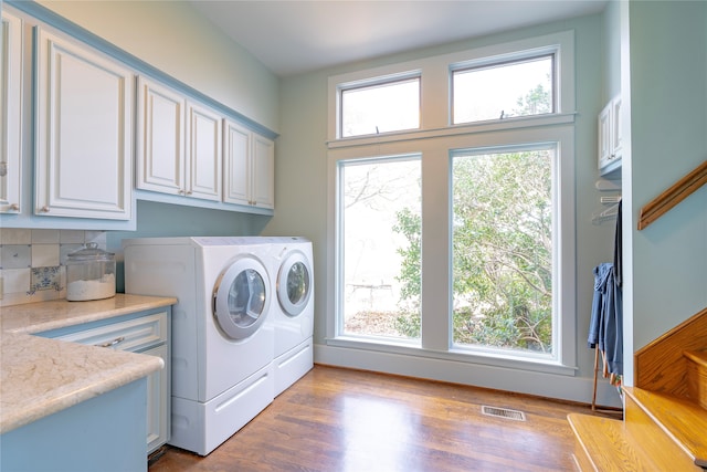 laundry room featuring cabinets, independent washer and dryer, light hardwood / wood-style floors, and a wealth of natural light