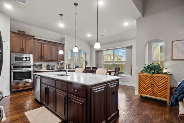 kitchen with pendant lighting, a center island with sink, sink, appliances with stainless steel finishes, and dark hardwood / wood-style flooring