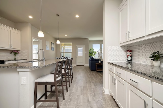 kitchen with stone counters, light wood-style floors, a kitchen breakfast bar, and a sink