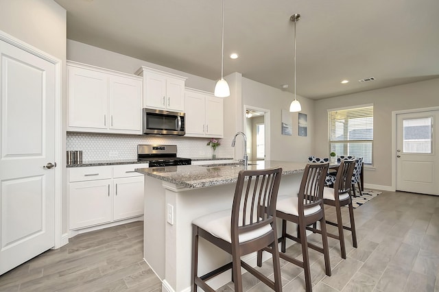 kitchen with visible vents, appliances with stainless steel finishes, a sink, stone counters, and backsplash