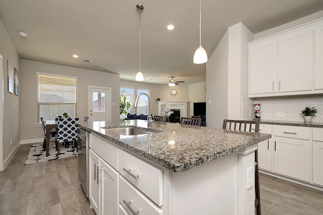 kitchen with pendant lighting, a sink, stainless steel dishwasher, light wood finished floors, and tasteful backsplash