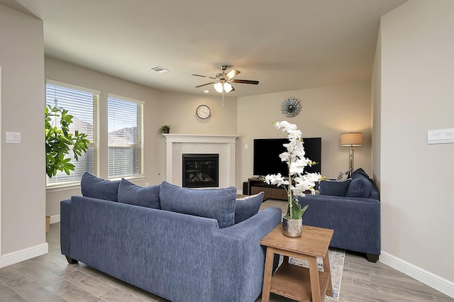 living room with a ceiling fan, a glass covered fireplace, visible vents, and baseboards