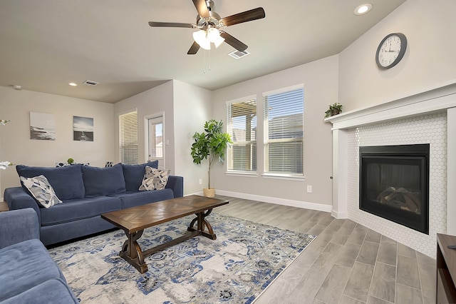 living room with baseboards, a tiled fireplace, visible vents, and wood finished floors