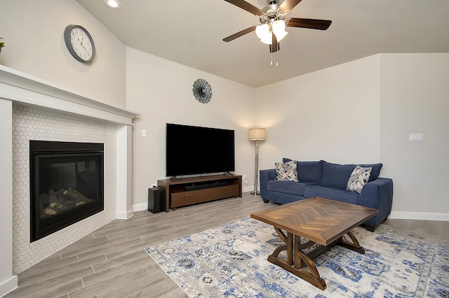 living room featuring a ceiling fan, wood tiled floor, a glass covered fireplace, and baseboards