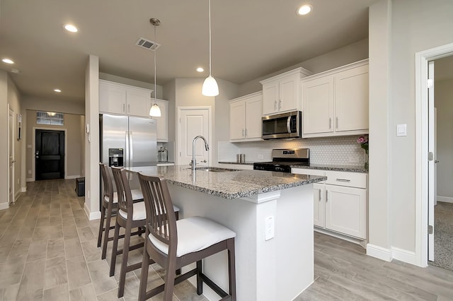 kitchen with stainless steel appliances, a kitchen island with sink, sink, pendant lighting, and white cabinetry