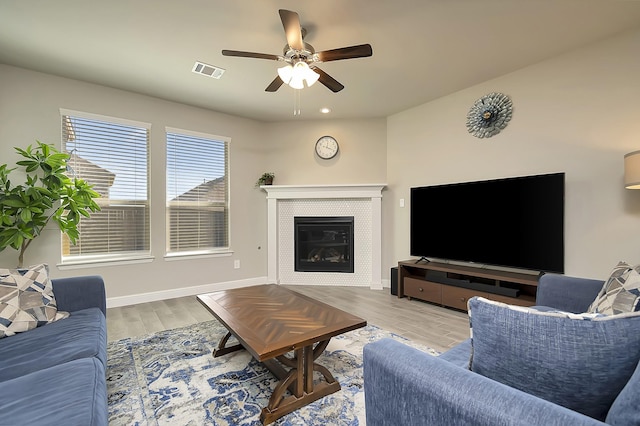 living room featuring a tile fireplace, ceiling fan, and light wood-type flooring