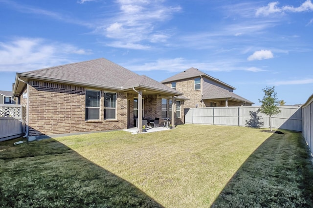 rear view of property featuring roof with shingles, brick siding, a lawn, a patio area, and a fenced backyard