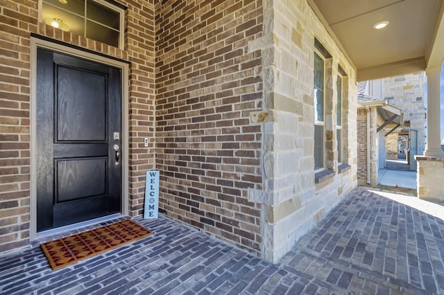 view of exterior entry featuring a porch and brick siding