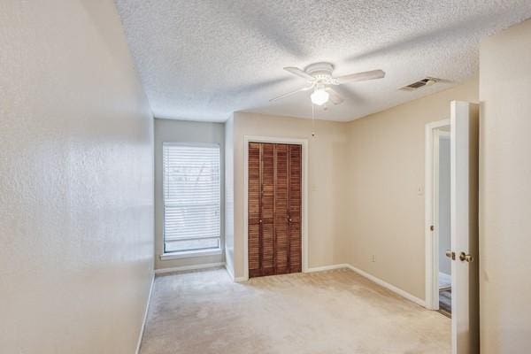 spare room with a textured ceiling, light colored carpet, and ceiling fan