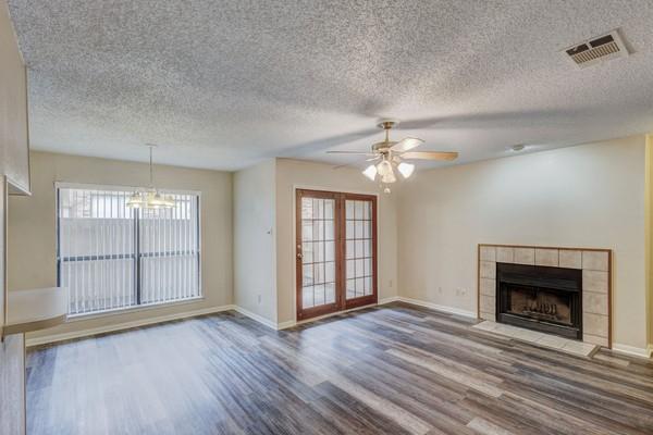 unfurnished living room with hardwood / wood-style floors, french doors, a textured ceiling, ceiling fan with notable chandelier, and a tile fireplace