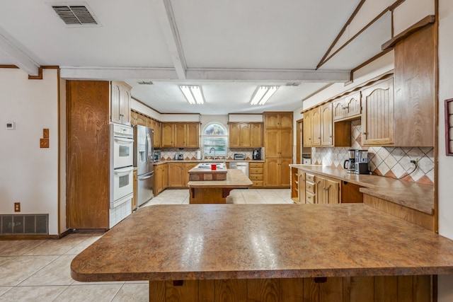 kitchen featuring backsplash, a kitchen island, light tile patterned floors, and appliances with stainless steel finishes