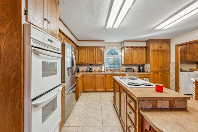 kitchen with sink, tasteful backsplash, a textured ceiling, white appliances, and light tile patterned floors