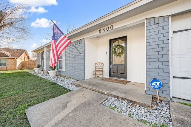 view of exterior entry featuring a garage, a yard, and brick siding