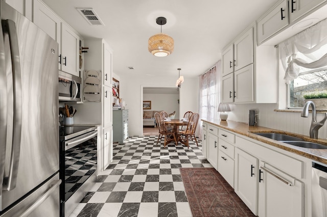 kitchen with dark floors, stainless steel appliances, a sink, visible vents, and white cabinetry