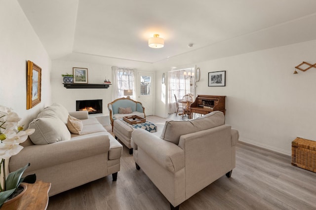 living area featuring a brick fireplace, wood finished floors, an inviting chandelier, and baseboards