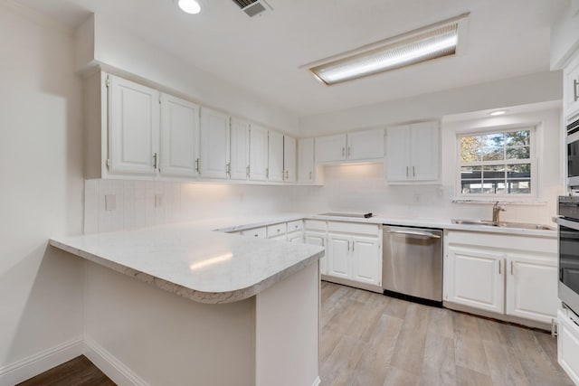 kitchen with stainless steel appliances, a peninsula, a sink, visible vents, and light wood finished floors