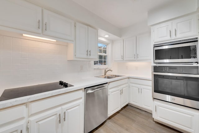 kitchen with light countertops, backsplash, light wood-style flooring, appliances with stainless steel finishes, and a sink