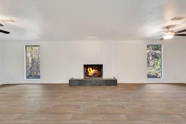 unfurnished living room featuring ceiling fan, a large fireplace, and light wood-type flooring