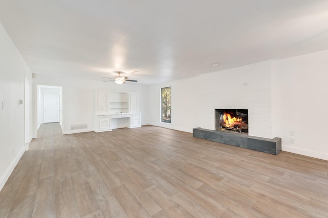 unfurnished living room with ceiling fan, a tiled fireplace, and light hardwood / wood-style flooring