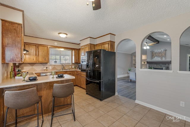 kitchen with kitchen peninsula, black fridge, a textured ceiling, ceiling fan, and a breakfast bar area