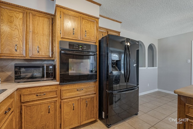 kitchen featuring backsplash, light tile patterned floors, black appliances, and a textured ceiling