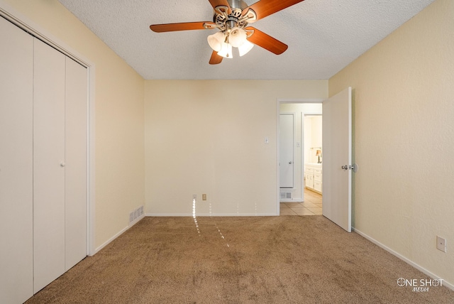 unfurnished bedroom featuring a closet, a textured ceiling, light colored carpet, and ceiling fan